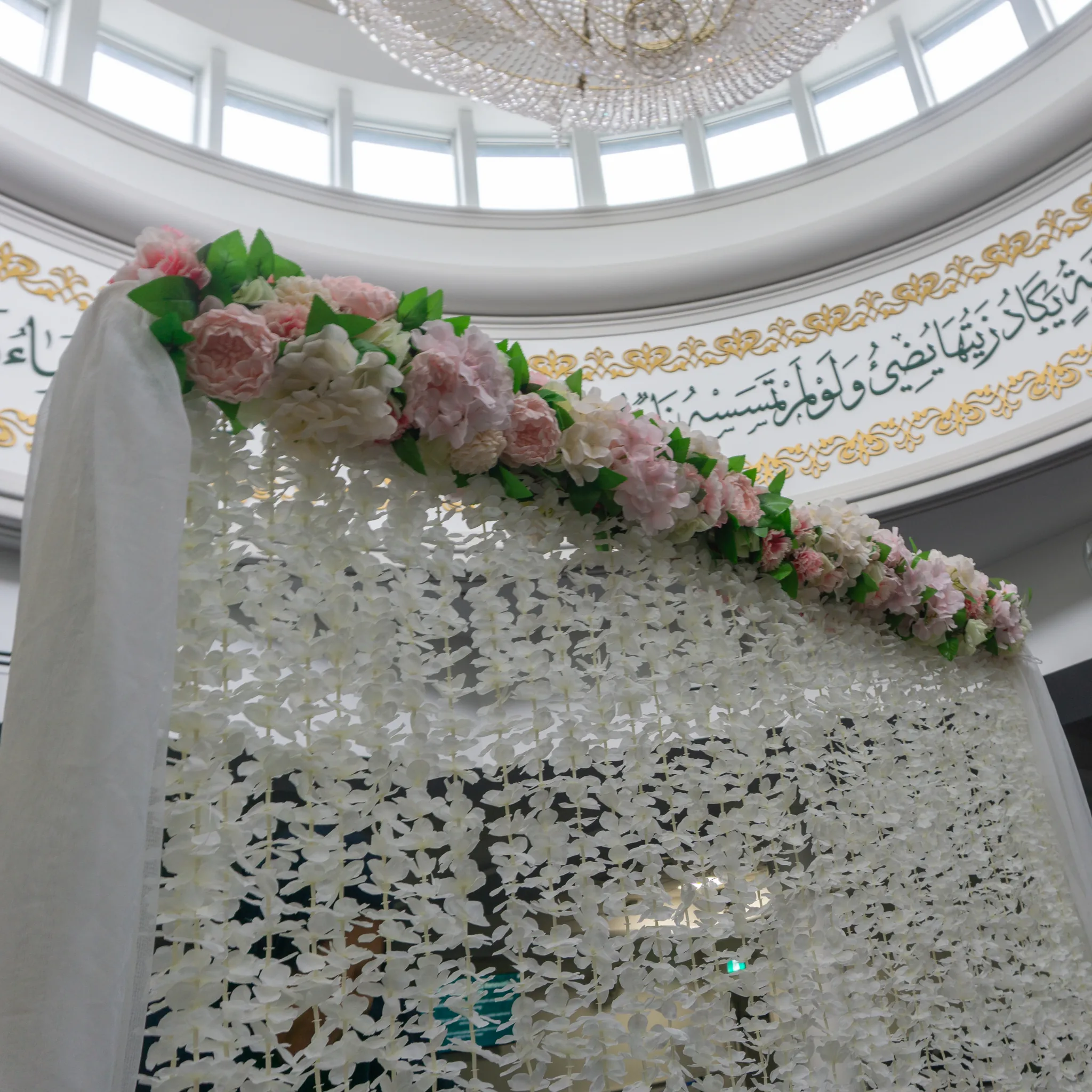 Looking up at the floral header and cascading petal strands beneath a masjid dome and chandelier