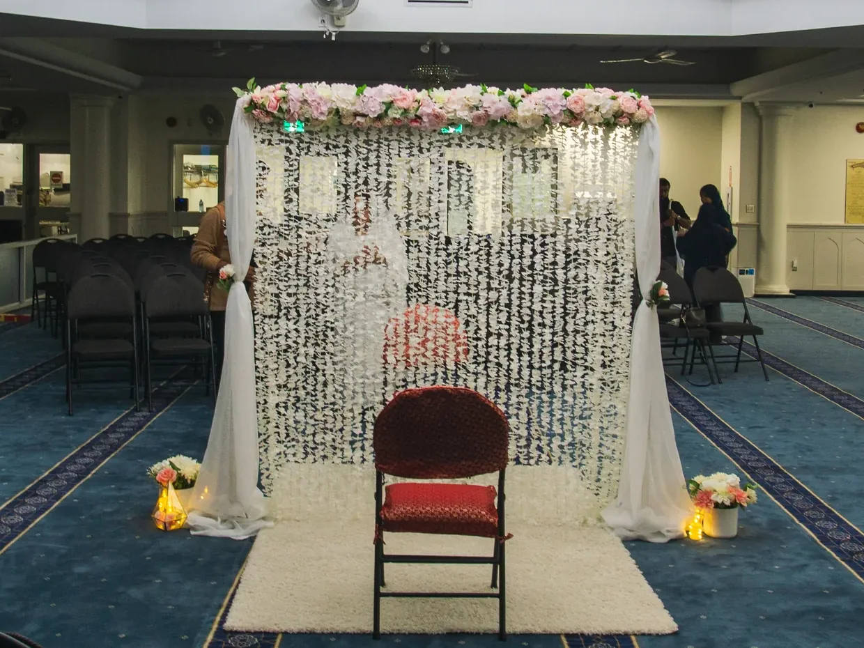 The Signature Stage Package: the wall in a masjid prayer hall, with a white rug underfoot, candles and floral arrangements