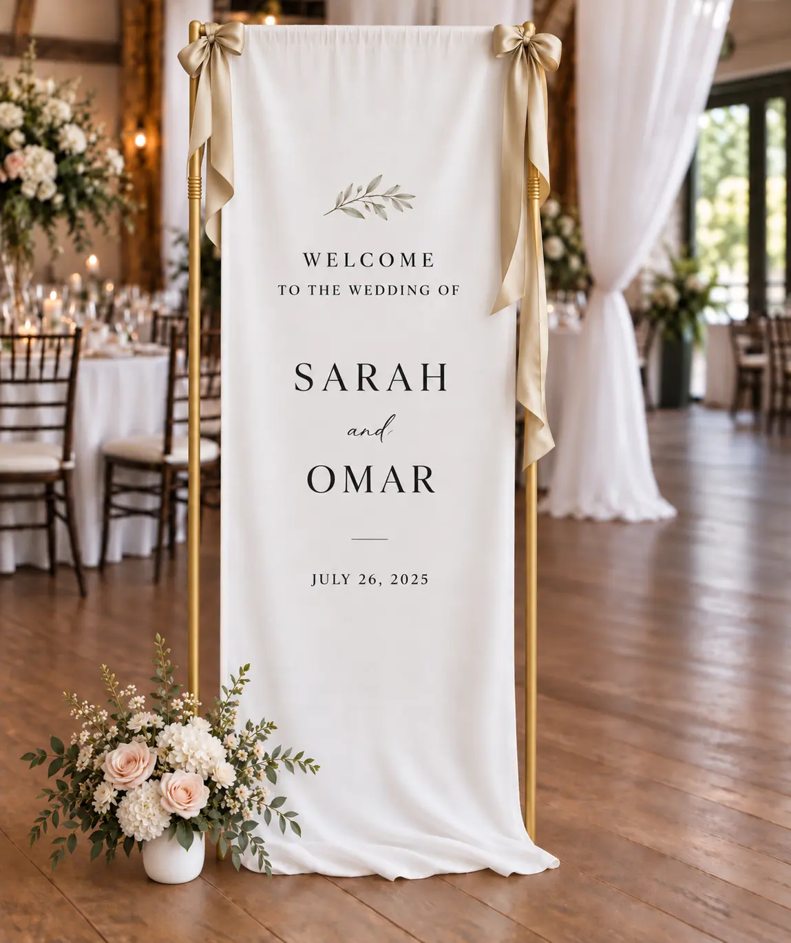 A linen welcome sign with names and a date, draped on a gold frame with satin bows and florals at its base