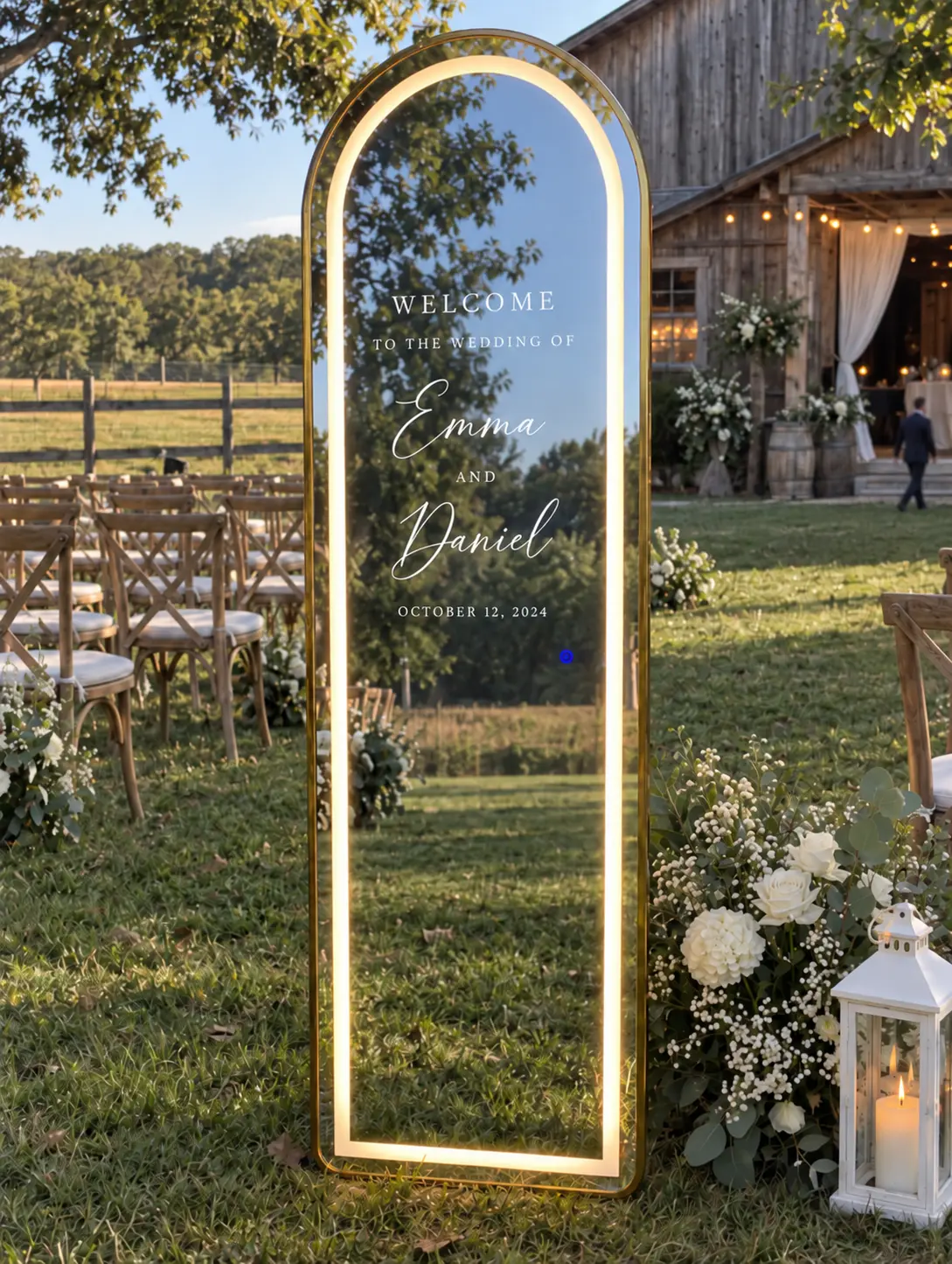 The LED arch welcome mirror on the lawn at an outdoor ceremony, beside white florals and a lantern